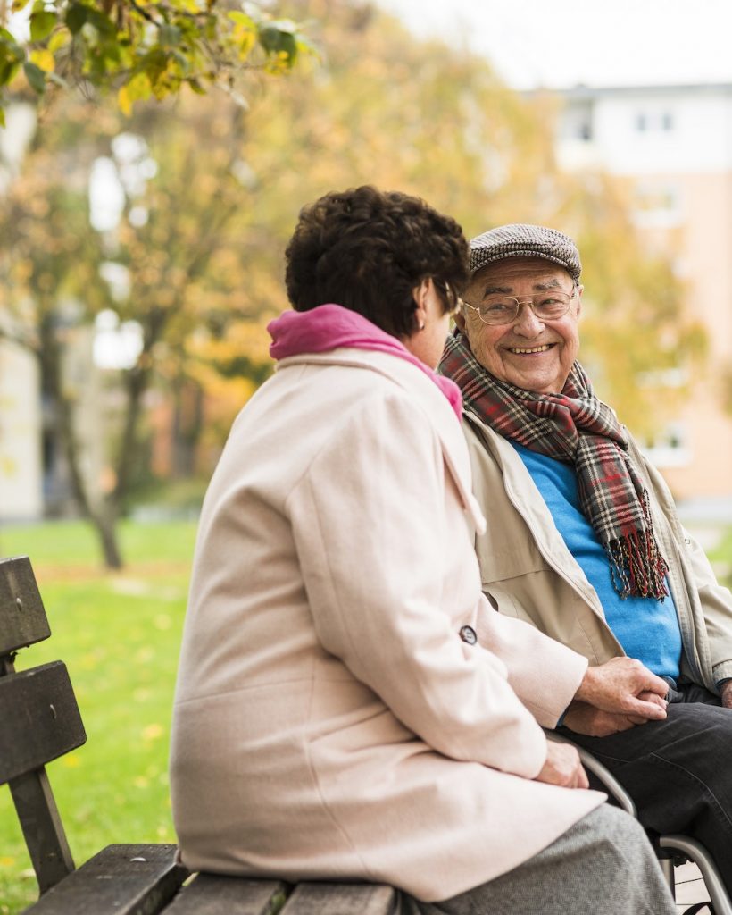 Senior man in wheelchair holding hands with wife on bench